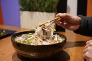 Pho vietnamien aux nouilles servi chez Omley Sushinem à Castelnau-le-Lez, main utilisant des baguettes,